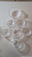 Top-down view of seven clear glass bowls arranged on a flat surface, showing floral starburst pattern on the base and scalloped edges.