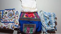 Three aprons laid out showing variety of colors and patterns including blue ethnic print, floral patterns, and white lace accents