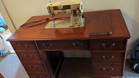 Full front view of the vintage brown wooden desk with integrated sewing machine compartment and sewing machine in place.