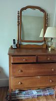 Front view of brown wooden dresser with attached mirror, showing four drawers and knob handles.