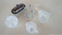 Top down view of 7 piece vintage crystal and metal tableware set including creamers, salt and pepper shakers, sugar bowl, and butter dishes on a plain background.