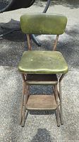 Front view of vintage chair with olive green worn plastic seat and backrest, metal frame with rust, and wooden lower step.
