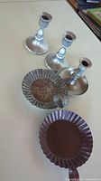Three pewter-style candlestick holders and two shallow tin dish candle holders on white surface, showing mixed colors and vintage character.