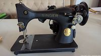 Side view of vintage Singer sewing machine showing black metal body, gold Singer logo, and mechanical parts.
