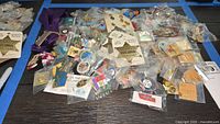 Wide view of the scattered pins on a table, showing many pins in individual plastic bags and some vintage display cards with pins attached.