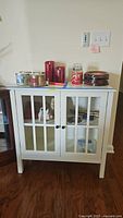 Front view of accent cabinet showing double glass panel doors, two knobs, and items on top (not included).