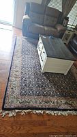 Full view of the Persian style area rug 6'x9' in a living room with fringed edges and detailed floral patterns under a coffee table and recliner couch.
