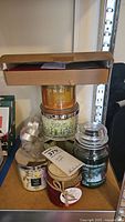 Various candles stacked including large jar candles and small decorative candles.