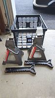 Pair of Pittsburgh 3 ton car stands with adjustable ratcheting arms and triangular black steel supports. Placed on floor next to plastic crate.