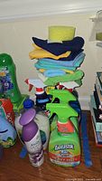 Multiple cleaning products and cloths stacked showing Fantastik, Softsoap, Febreze Light, and cleaning cloths