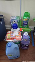 Photo showing various cleaning supplies on the floor including Gain Relax scent beads, Febreze large jug, Tide pods, Bounce dryer sheets, and Lysol bottle.
