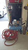 Full view of compressor, hoses, gauges, and rusty tank in garage space