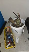 White bucket containing various copper pipes, brass fittings, and plumbing tools.