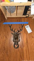 Full view of the metal elk door knocker showing the elk head with prominent antlers and round knocker ring on a wood floor.