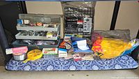 Photo of open plastic fishing tackle box showing lures, hooks, spools of line, and other fishing accessories spread out.