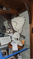 Detailed photo of large Great Horned Owl figurine with wings spread, on wooden base with nature-themed sculpted base, inside glass cabinet.