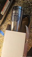 Stainless steel insulated travel mug with handle, in white box, branded with HVFC Brewing Co and brewery logo.