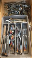Flatware set arranged in a drawer organizer showing knives, forks, large spoons, small spoons