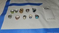 Ten assorted ladies rings displayed on white cloth with blue tape.