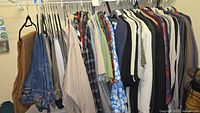 Full rack of assorted men's clothing: jackets, flannels, shirts, including denim and colorful patterns