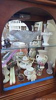Showcase cabinet with assorted decorative items including Coalport teapot, pressed glass bowl, iron Amish figurines, vases, miniature tea set, candles, and paperweights