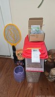 Lot items grouped together showing bug zapper, bird feeder on top of seed container, hose nozzle box, ceramic planter in front