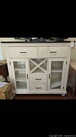 Front view of white wooden server showing drawers, cross wine rack, and glass door cabinets