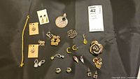 Overview of the lot arranged on black fabric showing earrings, pins, bracelet, and pendants.
