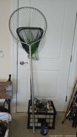 Two fishing nets with metal handles leaning against a door, a small table holding fishing reels and tackle boxes below.