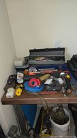 Full view of the workspace/table with blue toolbox and assorted tools, tape rolls, and hand tools scattered on the table surface and floor