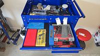 Top drawer with screwdriver set, small sockets set, and assorted blades and tools in blue tool cabinet drawer.