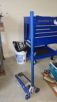 Floor jack upright next to blue tool chest and bucket