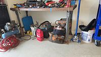 View of workbench and area beneath showing tools and equipment including compressor, tool bags, and welding machine.
