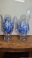 Front view of two blue and white spotted art glass flower vases with organic shaped petal rims and clear bases on wooden surface