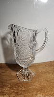 Clear lead glass crystal footed pitcher with hand cut frosted rose and geometric designs, hexagonal base, curved handle with dot detailing, and scalloped rim.