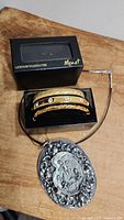 Set of three gold-tone Monet bangles with rhinestones, rope design detail, and plain finish in a box along with a silver-tone vintage pendant necklace with embossed scene on black cord.