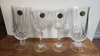 Four crystal glasses on a wooden table, 2 tall Cristal d'Arques Longchamp glasses and 2 smaller Cristal de Flandre wine glasses, all with original labels attached.