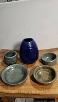 Photo showing the full handmade pottery set with all five pieces arranged on a wooden surface against a plain white wall.