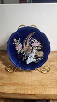 Front angle view of the cobalt blue porcelain plate with pheasant and floral design on a gold stand