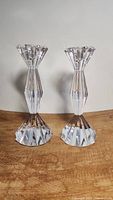 Pair of clear vintage crystal candlesticks with faceted geometric cuts shown from front, standing upright on wooden surface.
