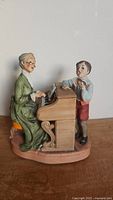 Side view of vintage figurine showing elderly woman playing piano with boy singing