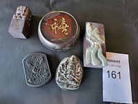 Overview photo of six Asian collectible stone items including a round ink stone with gold calligraphy lid, two rectangular carved seals, and three carved pendants with intricate designs.