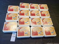 Fifteen Auto First Aid Kits laid out on a black surface, showing the white plastic cases with red labels.