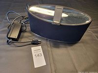 Side view of Bowers & Wilkins Zeppelin Mini speaker with power adapter and MaxSold tag number 143.