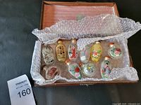 Wooden box containing 10 Chinese snuff bottles cushioned with bubble wrap, showing various shapes and painted designs.