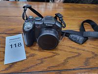 Front view of Canon PowerShot S3 IS camera with lens cap and neck strap on wooden table.