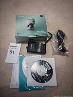 Top-down view of lot: camera, original box, cables, software CD and printed guides.