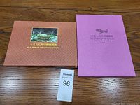 Photo showing two stamp sets closed: a brown-orange album and a purple booklet on a wood table.