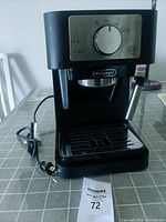 Front view of Delonghi espresso machine showing control knob, steam wand, power cord, and drip tray.