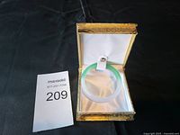 Light green and white jade bracelet inside a gold-colored decorative box with white satin lining